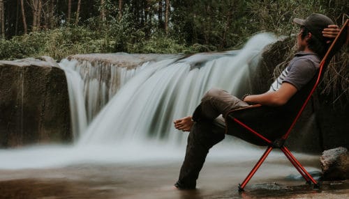 Man sitting in a folding camping chair next to a waterfall