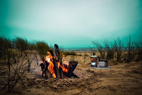 Small folding camping tables can be taken anywhere and have a ton of different uses. Small folding camping table on a beach next to a campfire.