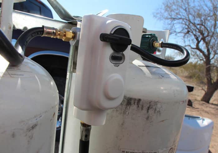 RV propane regulator near two propane tanks on a travel trailer