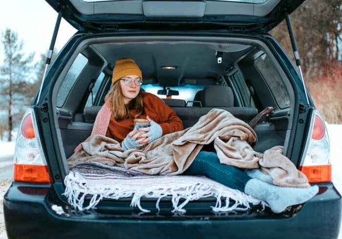 woman camping in a car using a portable heated blanket that's powered by a portable power station during traveel