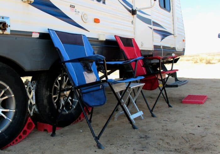 aluminum folding small compact camping table next to camp chairs and an rv travel trailer