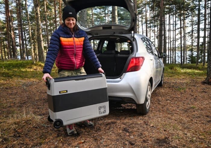 vevor portable refrigerator 12 volt fridge freezer being carried from the trunk of a car