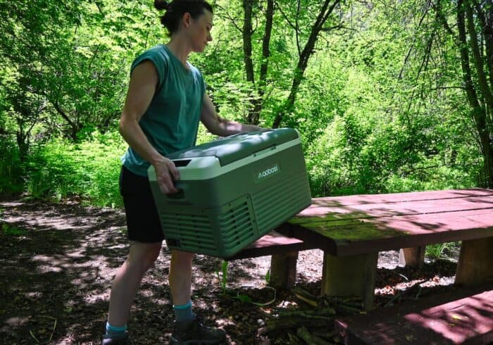 woman putting an Aaobosi portable fridge on a picnic table while camping 