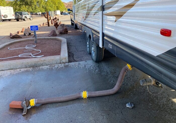 RV connected to a dump station with a sewer hose draining waste tanks beside a safe drinking water spigot.
