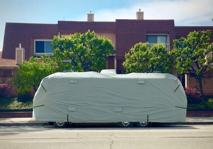 Class A RV covered with a heavy-duty gray motorhome cover designed for full weather protection, parked on a suburban street, ideal example of how to protect a motorhome from UV rays, rain, and wind.
