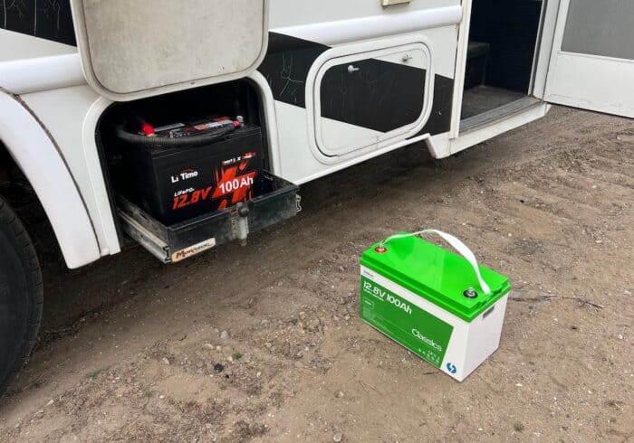Lithium RV battery mounted in an exterior tray with a second 12.8V 100Ah battery sitting beside the motorhome